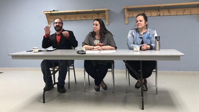 Un homme et deux femmes sont assis derrière une table durant un point de presse.