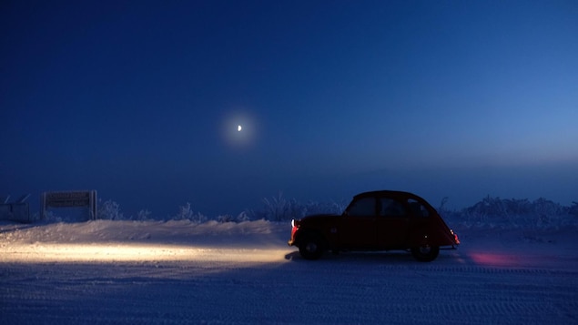 La Citroën 2 CV circule la nuit les phares allumés sur une route enneigée dans le nord du Canada La Citroën 2 CV circule la nuit les phares allumés sur une route enneigée dans le nord du Canada
