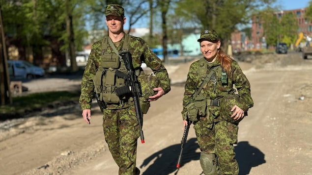 Un homme et une femme qui portent un treillis militaire et une arme en bandoulière marchent côte à côte.
