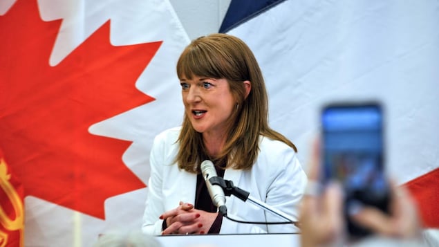 Claire Johnson derrière un micro devant des drapeaux du Canada et de l'Acadie, le 1er juin 2026 à Moncton.