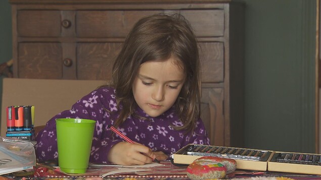 Clara dessine à une table, entourée de crayons de couleur. Clara dessine à une table, entourée de crayons de couleur.
