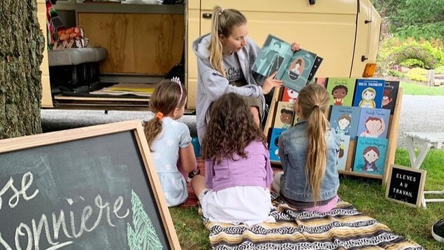 Une enseignante lit un livre à un groupe d'enfants devant un Westfalia dans un parc.