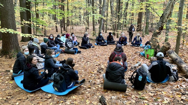Des étudiants assis en rond sur des tapis dans une forêt.