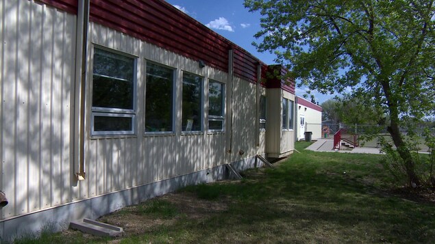 Façade extérieur de classes portatives avec un arbre et un parc pour enfants à l'arrière. Façade extérieur de classes portatives avec un arbre et un parc pour enfants à l'arrière.