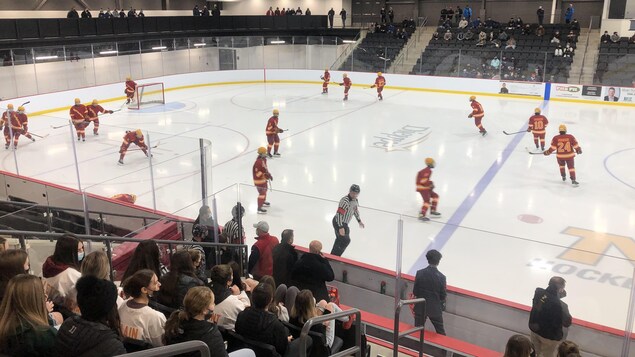 Des joueurs de hockey sur une patinoire devant des spectateurs assis dans des gradins.