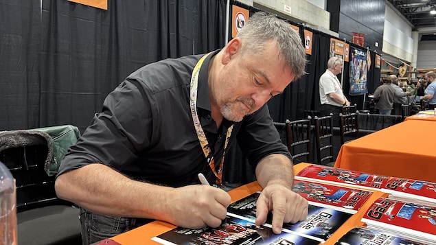 Claude Legault signe un autographe sur une affiche d'une Galaxie près de chez vous.