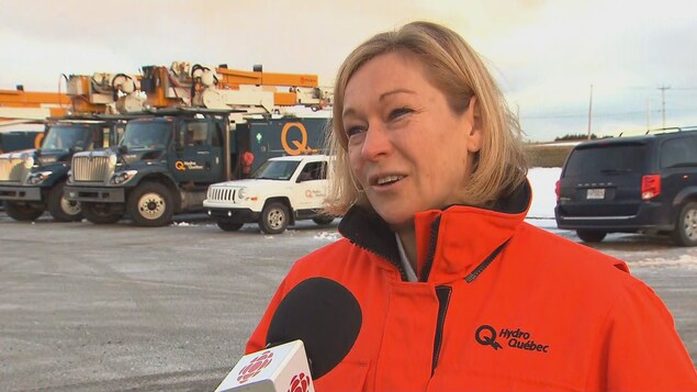 Elle répond aux questions d'un journaliste. Derrière elle, plusieurs camions d'Hydro-Québec sont stationnés.