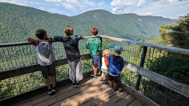 Des enfants se trouvent au sommet d'une montagne, sur une plateforme en bois. 