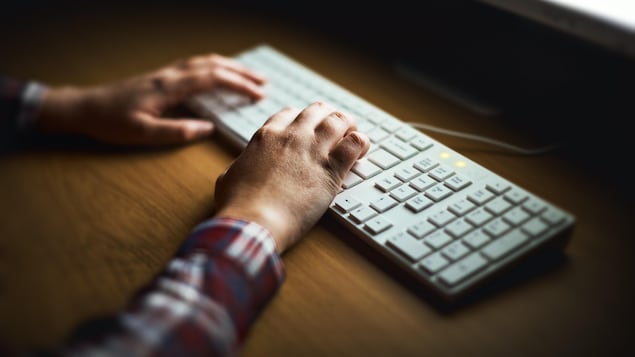 Mains d'un homme qui tape sur un clavier d'ordinateur.
