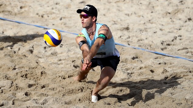 Un joueur qui se penche pour frapper un ballon de volleyball sur une plage lors d'une rencontre.