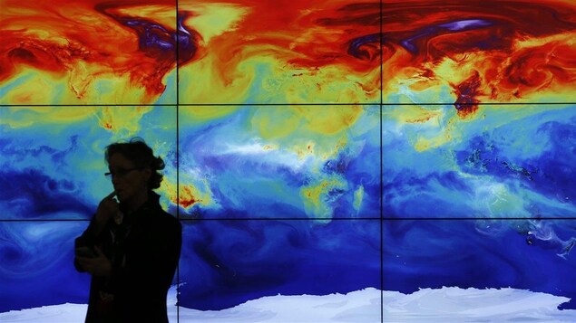 Une femme devant une carte numérique du monde qui montre les variations de températures. 