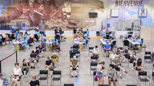 Des gens attendent dans une grande salle d'une clinique de vaccination, à Montréal.
