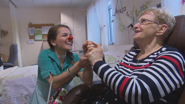 Une clown prend la main d'une dame âgée. Les deux sourient.