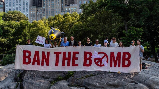 Des manifestants tiennent une bannière contre l'arme nucléaire. On y lit : « Ban the bomb ».