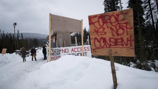 People walking on a road with signs planted in the snow.