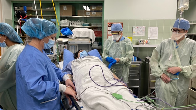 Una mujer yace en una cama de hospital en un quirófano, rodeada de personal médico.
