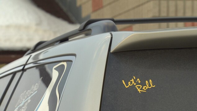 Un collant jaune « Let's Roll » sur la vitre arrière d'une voiture. Un collant jaune « Let's Roll » sur la vitre arrière d'une voiture.