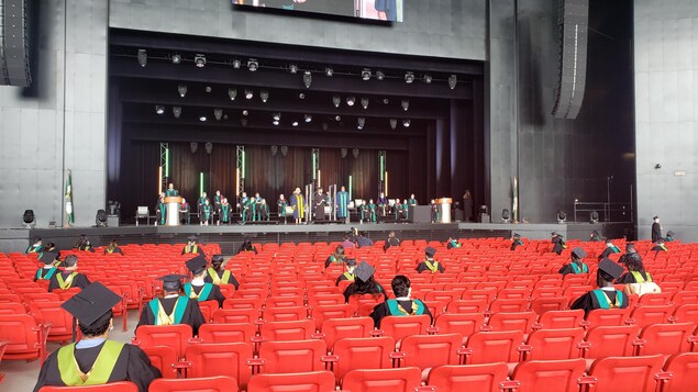 Des étudiants universitaires avec toge et mortier assis dans la salle à une grande distance.