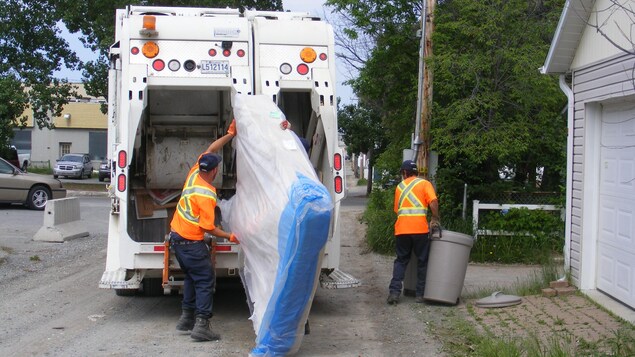 Un employé hisse un matelas dans un camion à déchets.