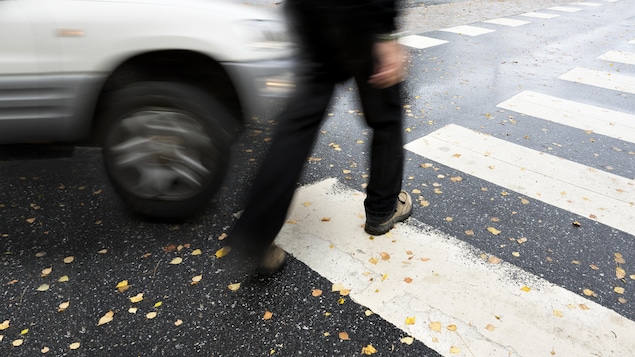 Un piéton marche sur une traverse alors qu'un véhicule passe rapidement à côté de lui.