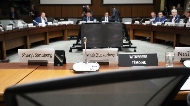 Les noms de Sheryl Sandberg et de Mark Zuckerberg sont affichés, devant des chaises vides.