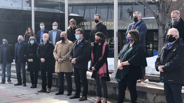Les élus sont debout devant les drapeaux en berne de l'Hôtel de ville de Gatineau.