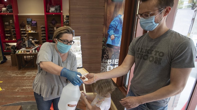 Une femme portant un masque désinfecte les mains d'un client qui, lui aussi, porte un masque.