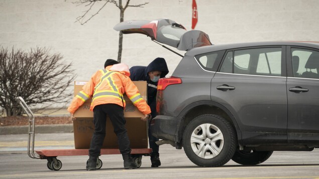 Un employé de quincaillerie aide un homme à mettre une boîte dans le coffre de sa voiture dans un stationnement.