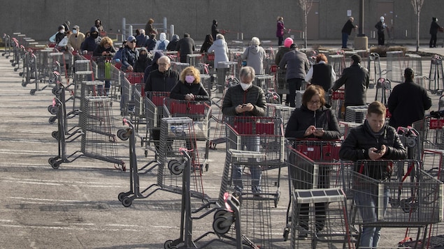 Des clients font la file avec des paniers dans le stationnement d'un commerce.