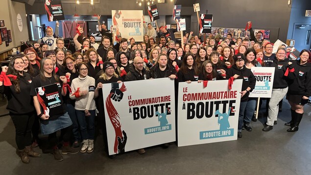Des dizaines de personnes issues d'organismes communautaires prennent une photo de groupe en tenant des affiches.