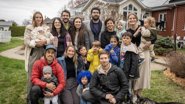 Dix adultes, neuf enfants et un chien devant une résidence.