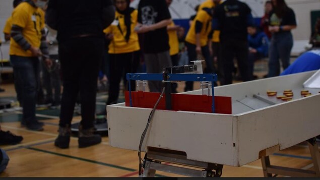 Des jeunes à l'arrière-plan déploient leurs robots alors qu'on en voit un à l'avant-plan.  