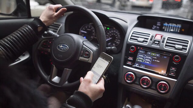 Un conducteur de voiture tient son téléphone cellulaire en conduisant.