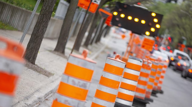Des cônes orange et une flèche clignotante détournent la circulation près d'un chantier de construction.