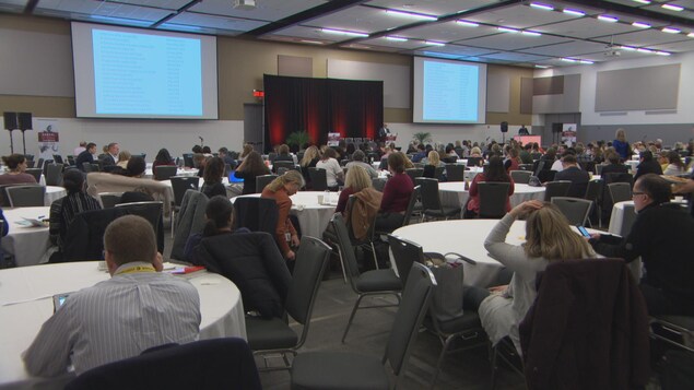 Des gens regardent un conférencier dans une grande salle. Des gens regardent un conférencier dans une grande salle.