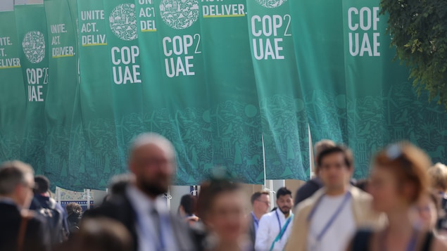 Des délégués marchent devant des banderoles de la COP28. 