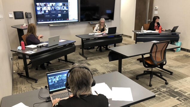 Trois personnes dans une salle de conférence, chacune à son bureau, participe à un appel conférence vidéo.