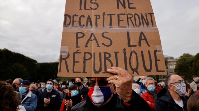 Une personne brandit une pancarte sur lequel on peut lire « Ils ne décapiteront pas la République ».