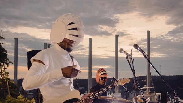 Deux musiciens portant un casque entrouvert à plusieurs endroits jouent sur une terrasse. Le mont Royal est visible au loin.