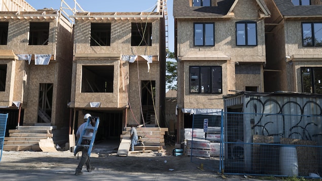 Un ouvrier, escabeau sur l'épaule, se dirige vers des maisons en chantier à Toronto.