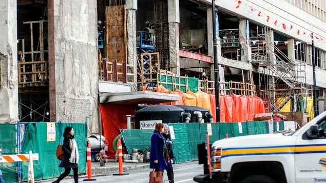 Un chantier de construction est ouvert sur la rue à la vue des passants et à côté de voies de circulation.