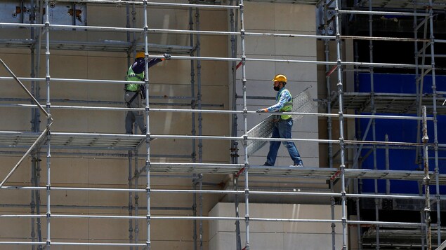 Deux travailleurs de la construction circulent sur un échafaudage le long d'un édifice.
