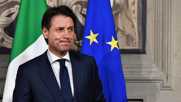 Giuseppe Conte, la mine basse, devant des drapeaux de l'Italie et de l'Union européenne. Giuseppe Conte, la mine basse, devant des drapeaux de l'Italie et de l'Union européenne.