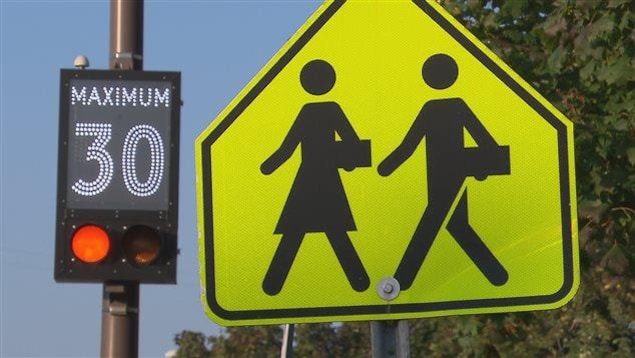 Deux panneaux, un illuminé montrant la vitesse permise et l'autre jaune arborant deux enfants qui marchent.