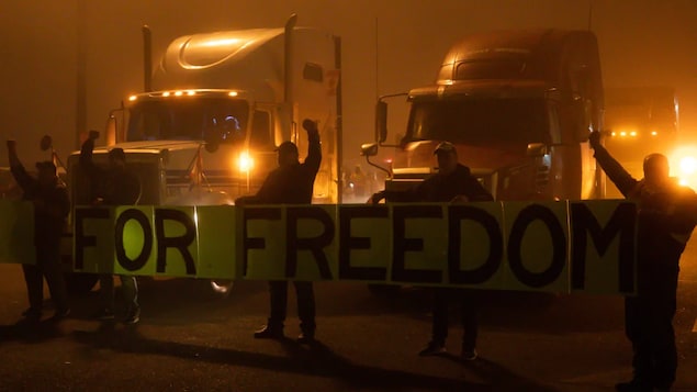 People hold a banner reading “for freedom” in front of trucks.