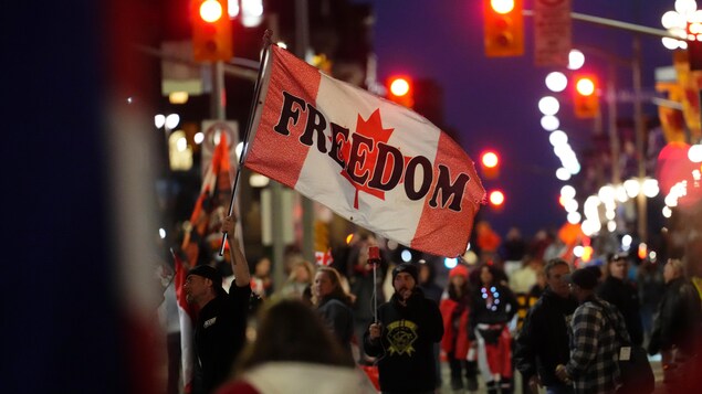 A man is holding a flag of Canada where it also says "Freedom".