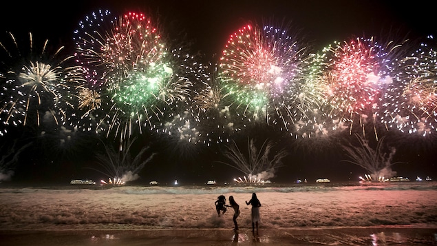 Des personnes célèbrent le Nouvel An sur la plage de Copacabana, aavec en arrière-plan de nombreux feux d'artifice.