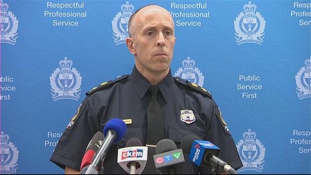 Corey Zaharuk, un homme fin au visage grave et triste, en uniforme de police, se tient devant des micros pour une conférence de presse. Corey Zaharuk, un homme fin au visage grave et triste, en uniforme de police, se tient devant des micros pour une conférence de presse.
