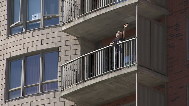 Un homme sur son balcon salue des personnes en brandissant sa main.