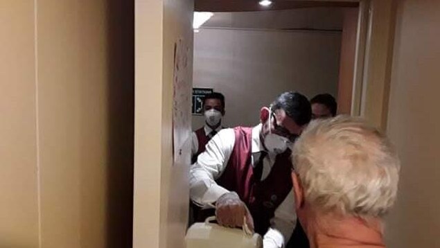 Du personnel d'un navire de croisière verse du café à un homme dans sa cabine.
